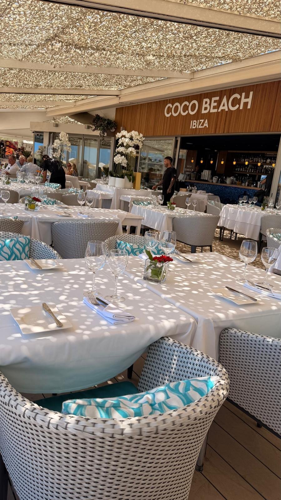 Coco Beach Ibiza restaurant terrace with white tablecloths and turquoise cushions under a shaded canopy